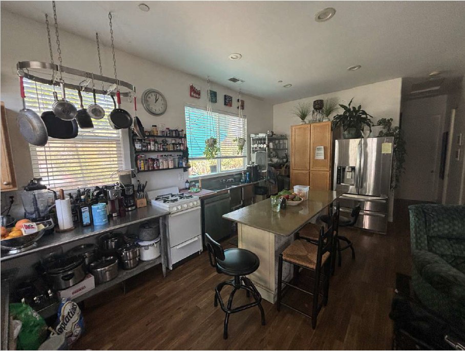 Original utility kitchen with industrial prep table, gas range, pot rack, and entertainment center used as an island